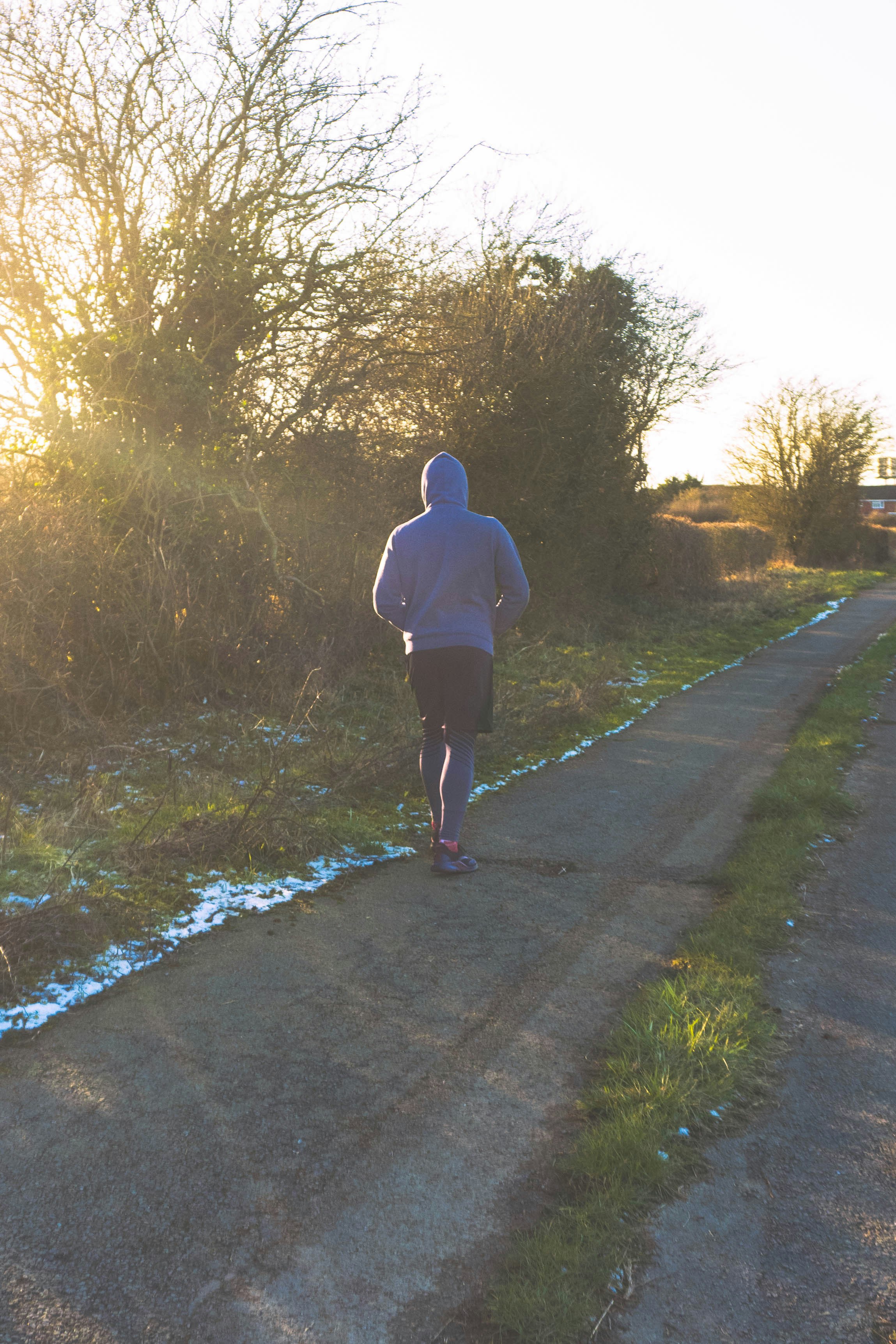 man running outside wearing hoodie sun shining through trees